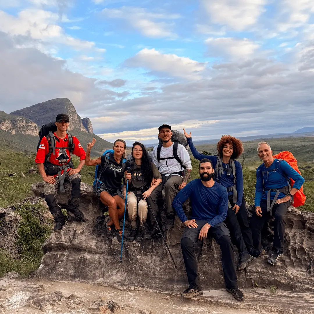 Grupo de trilheiros com mochilas se prepara para iniciar o trekking no Vale do Pati, Chapada Diamantina, diante de montanhas e céu azul com nuvens