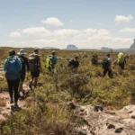 Pessoas caminham no gerais do rio Preto em meio a montanhas e vegetação rasteira, no Vale do Pati