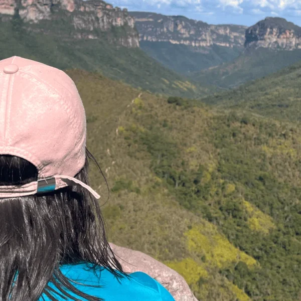 Mulher de costas aprecia Mirante do Vale do Pati durante trilha. Vegetação e Morros ao fundo